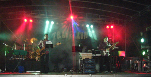 El Grupo Trávelling tocando en un escenario iluminado con focos rojos y verdes